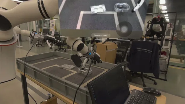 Robot gripper above metal parts in a tray, with a top-down teleoperation overlay.