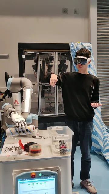 Operator in a Vision Pro teleoperating a UR arm with a dexterous hand holding a paint roller.